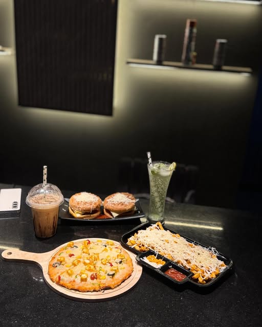 A spread at TeaXpresso: iced coffee, cheese burgers, a personal wood-fired pizza and loaded cheese fries on a dark counter.